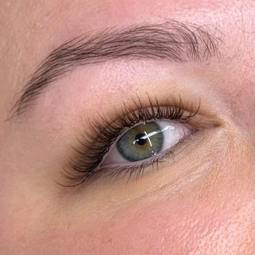 Close-up of a human eye with light makeup, long lashes, and well-groomed eyebrow.