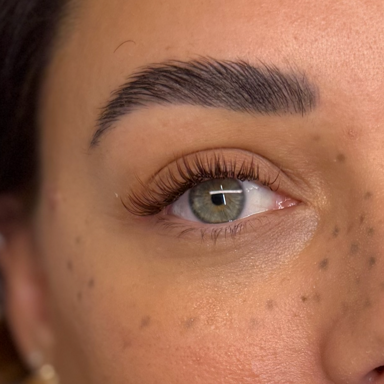 Close-up of a person's eye with gray-green iris, long eyelashes, and well-groomed eyebrow.