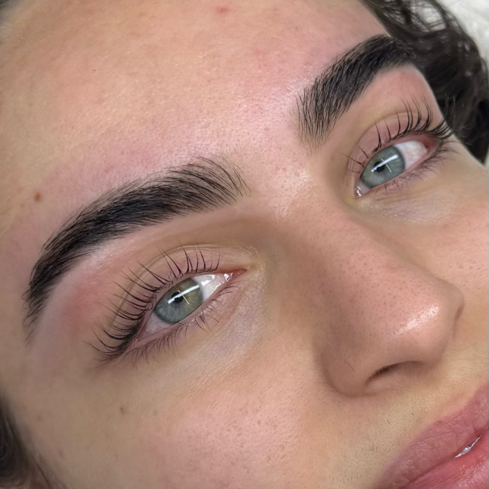 Close-up of a woman's face highlighting her groomed eyebrows, long eyelashes, and clear blue eyes.