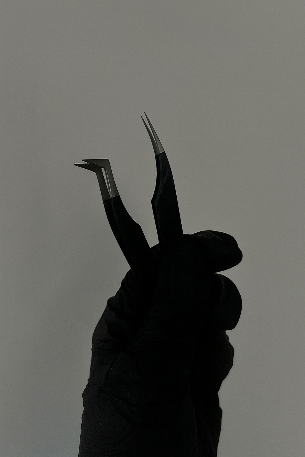Close-up of a gloved hand holding a pair of eyelash extension tweezers against a neutral background.