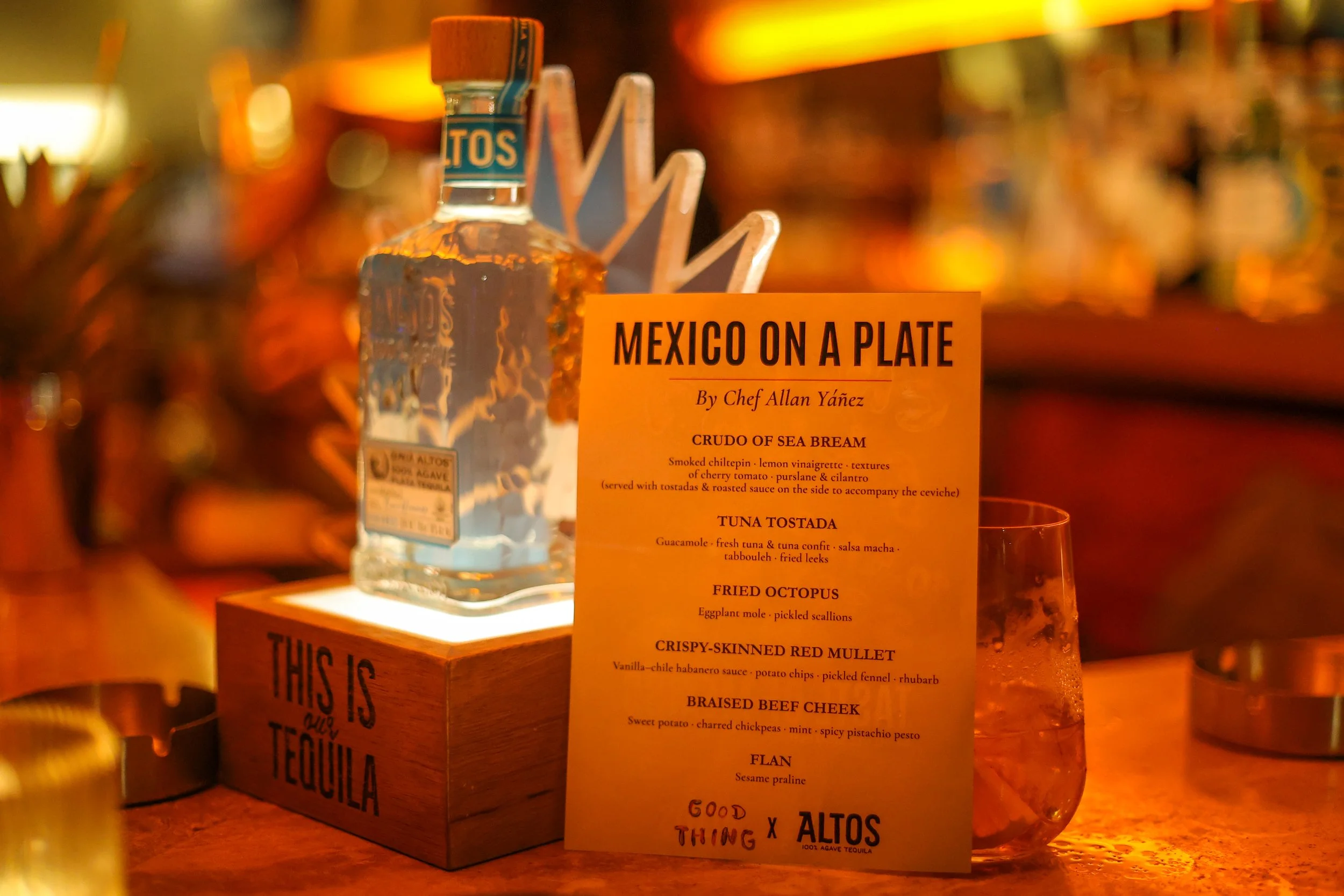 A menu titled 'Mexico on a Plate' by Chef Allan Yáñez, featuring dishes such as Crudo of Sea Bream, Tuna Tostada, Fried Octopus, Crispy-Skinned Red Mullet, Braised Beef Cheek, and Flan, with a bottle of Altos tequila in the background.