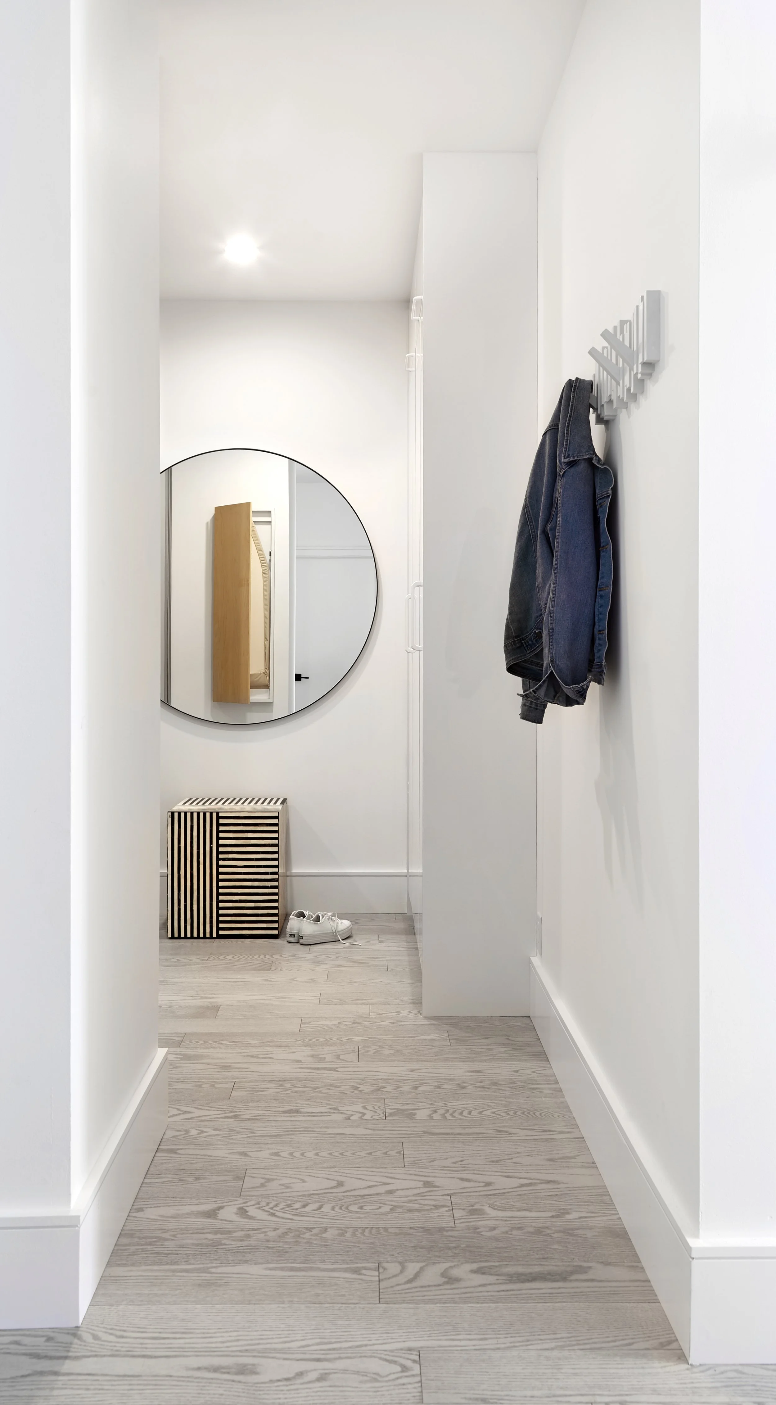 Minimalist hallway with a round mirror, hooks for your everyday wear, and a statement stool. 