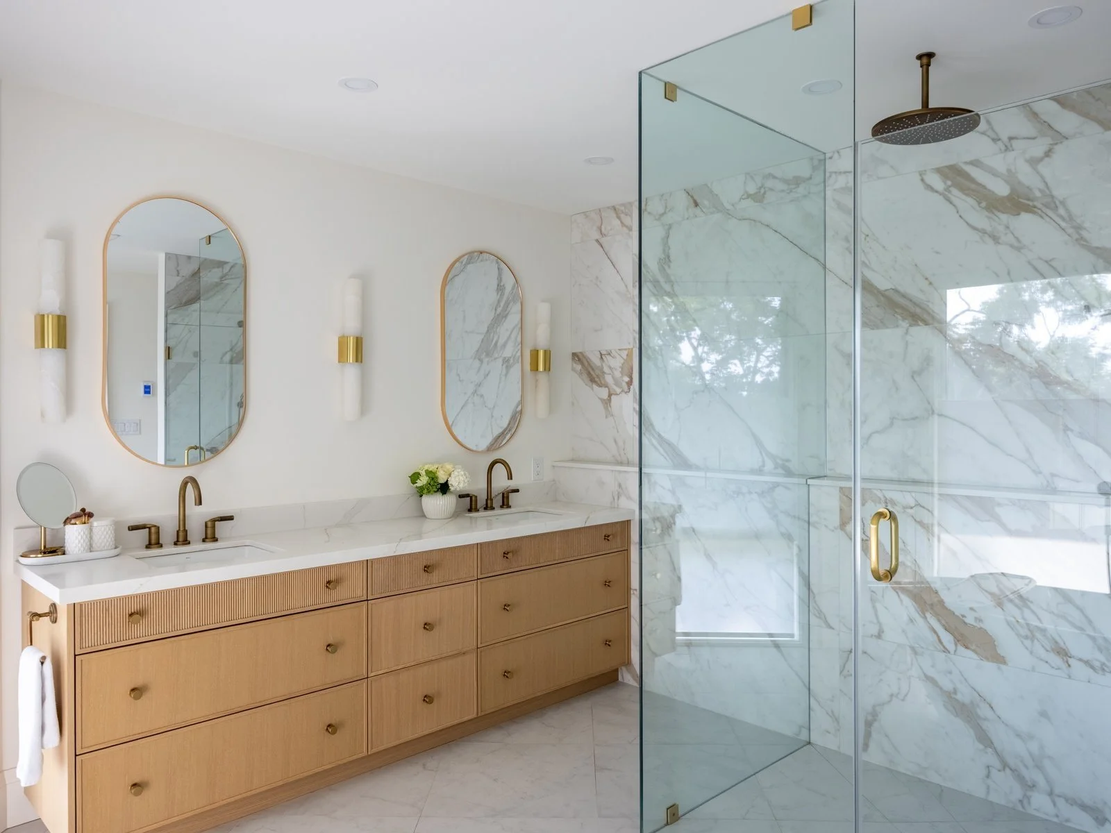Modern bathroom with double vanity, marble countertops, and a glass-enclosed walk-in shower with marble walls.