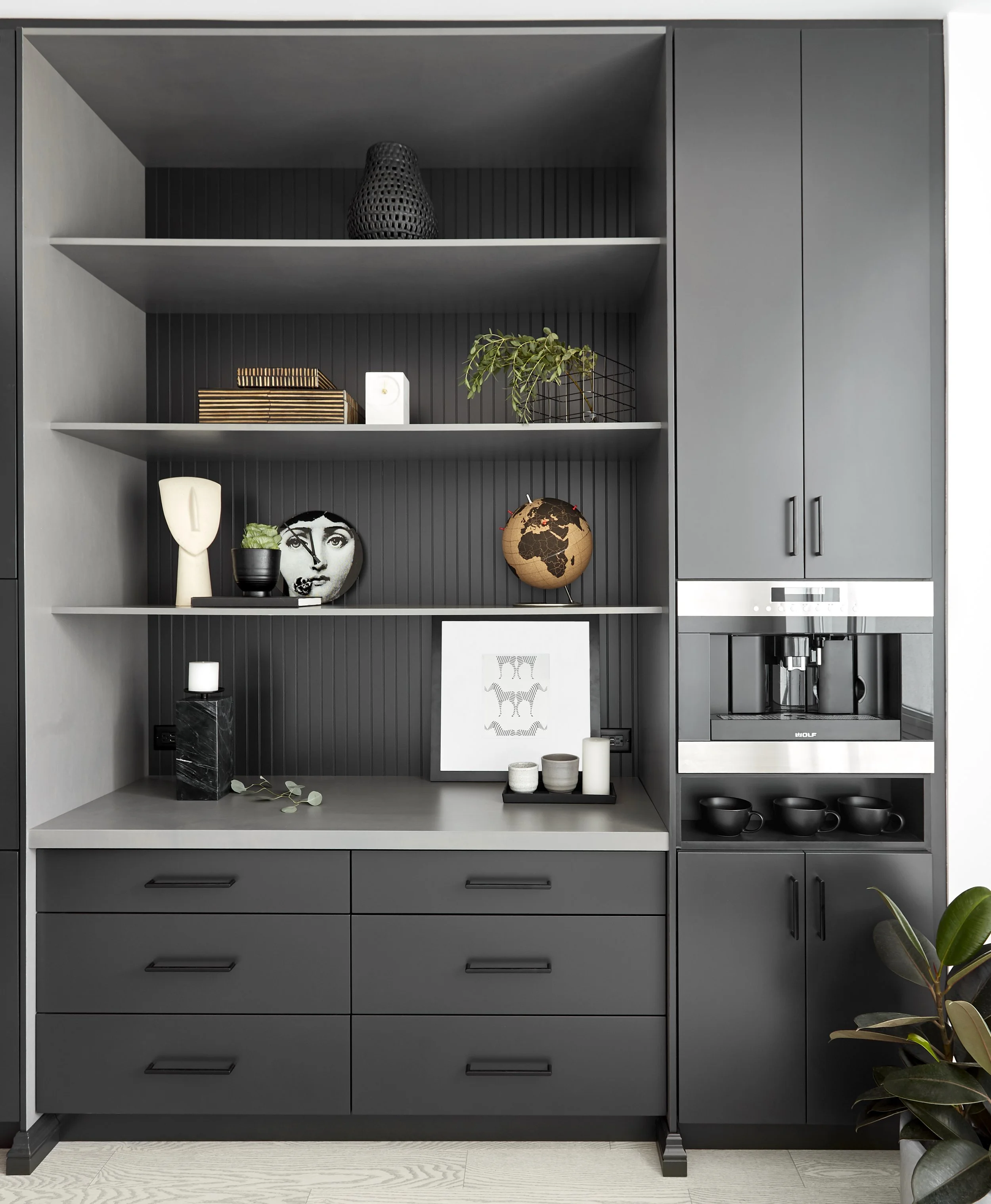 Modern kitchen cabinet with open shelves displaying decorative objects, plants, and a coffee maker, in a sleek gray color scheme.