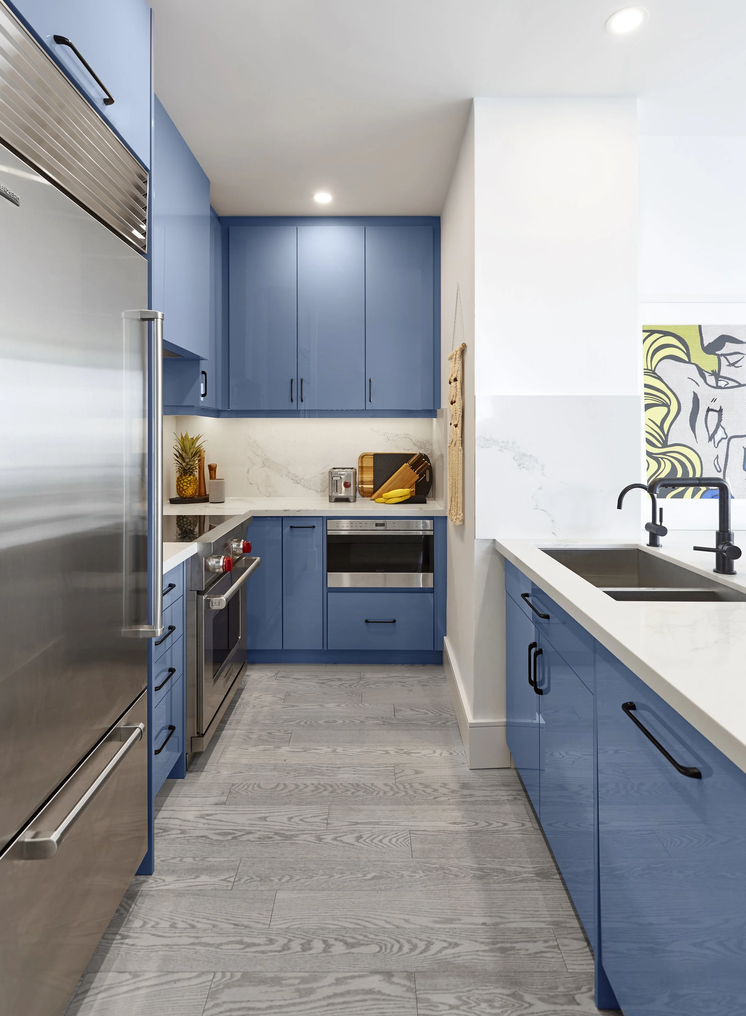 Modern kitchen with blue cabinets, stainless steel appliances, white countertops, and a wood floor.