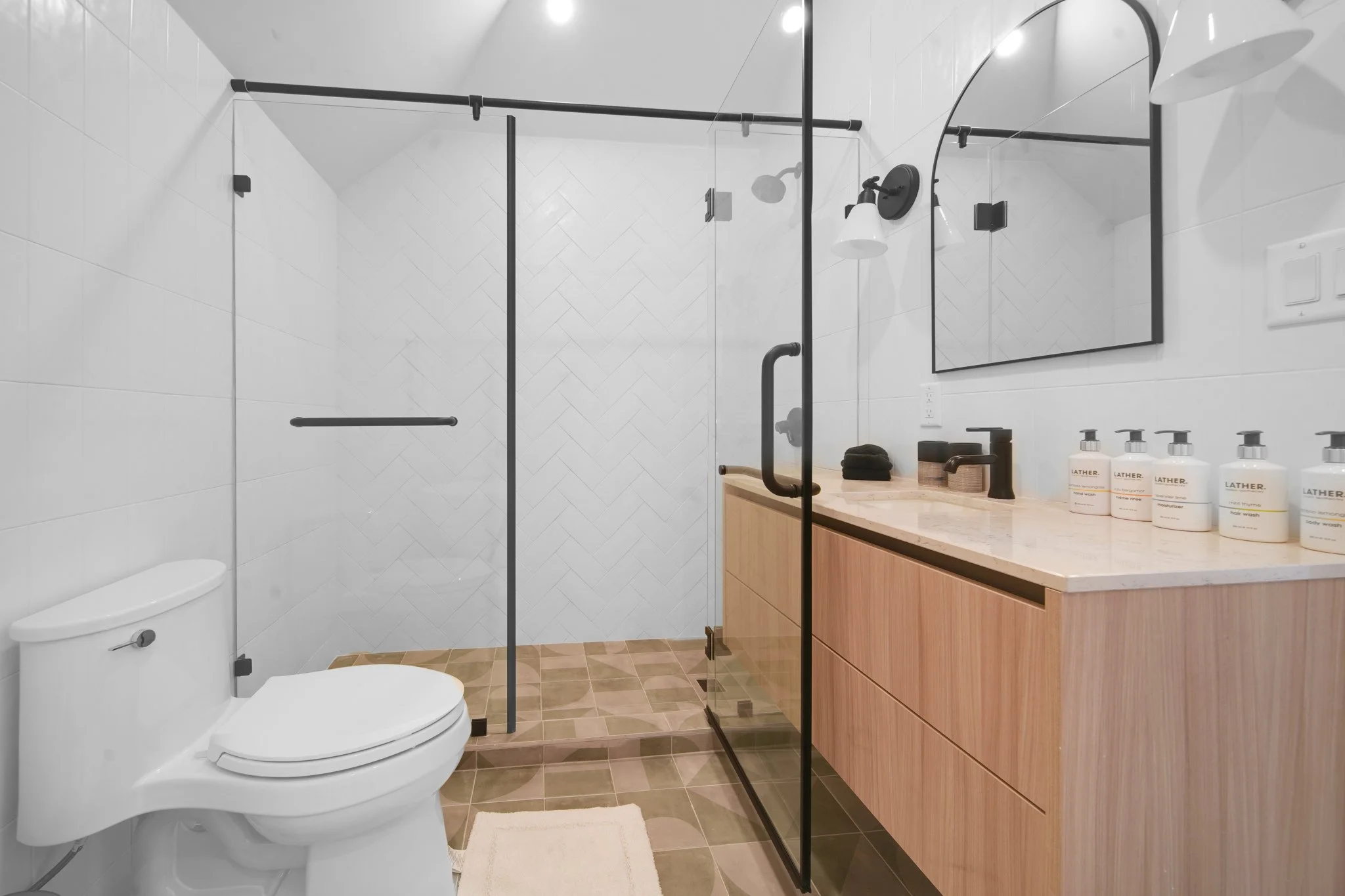 Modern bathroom featuring a glass shower enclosure, white toilet, a wooden vanity with black fixtures, and a large mirror with black trim.