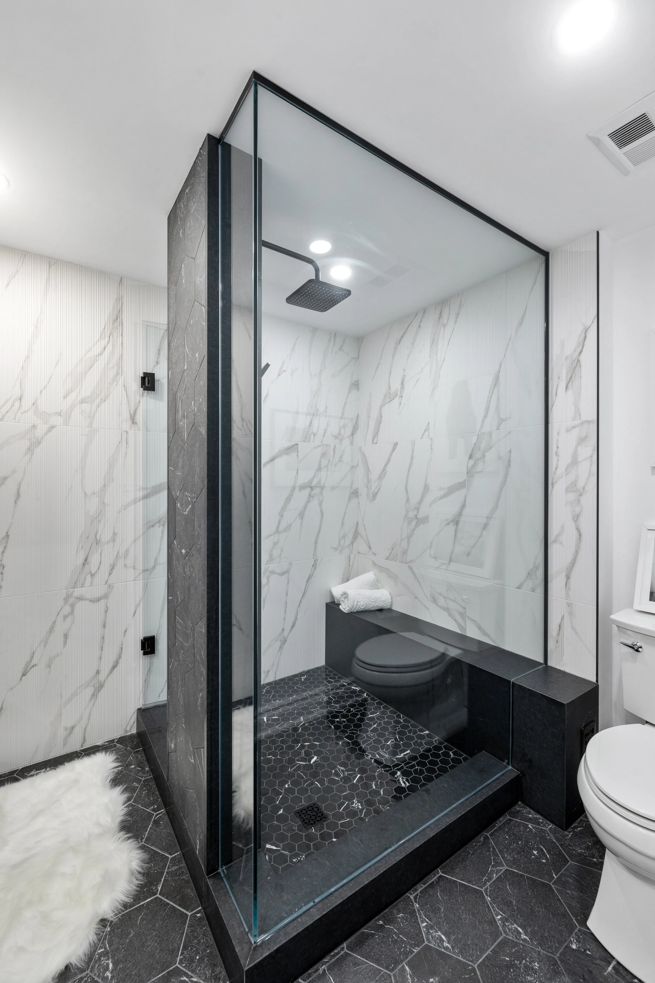 Modern bathroom with a glass-enclosed shower featuring black and white marble tiles, a rainfall showerhead, and a white toilet.