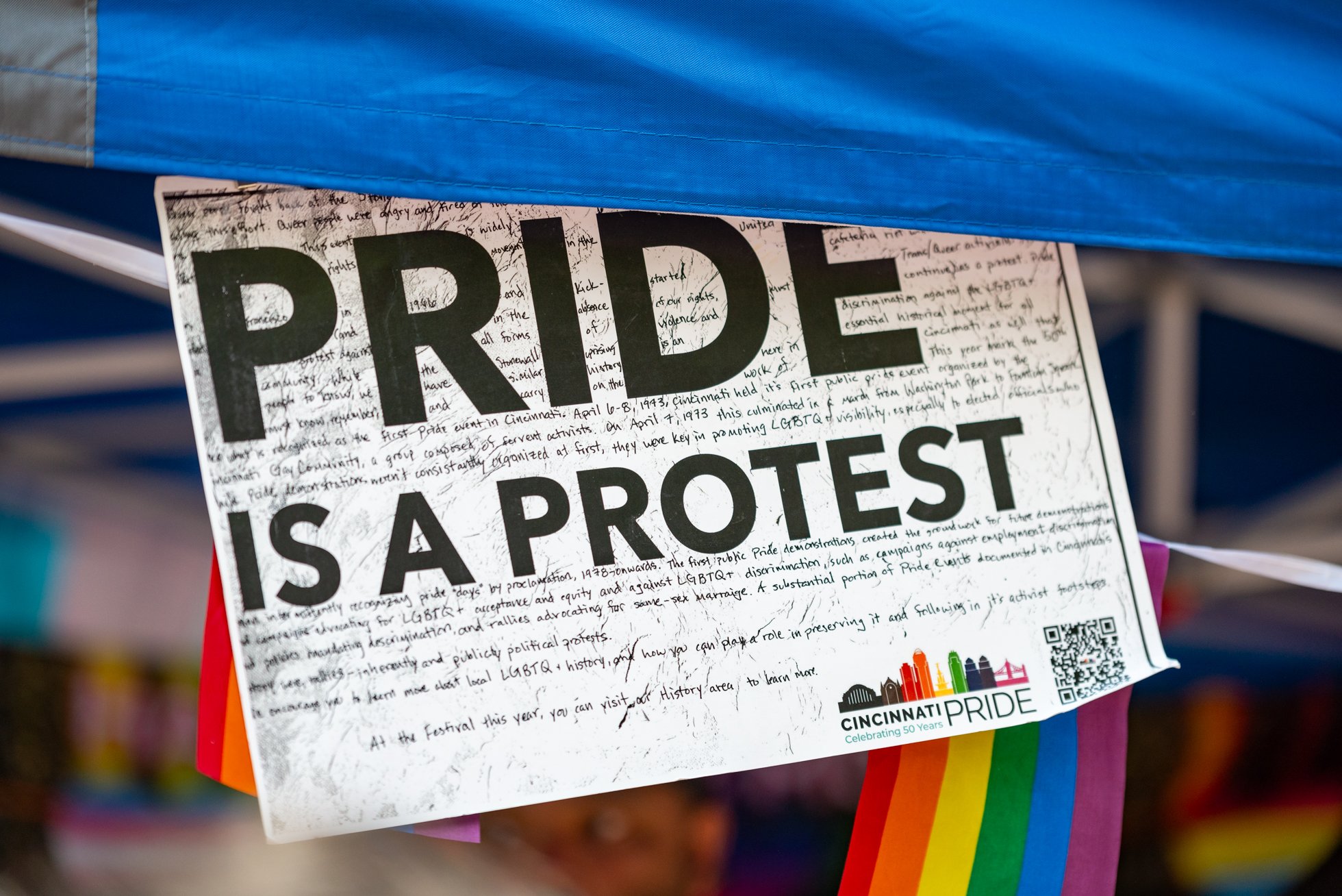 Poster with bold text reading 'PRIDE IS A PROTEST' and rainbow flags at the bottom.
