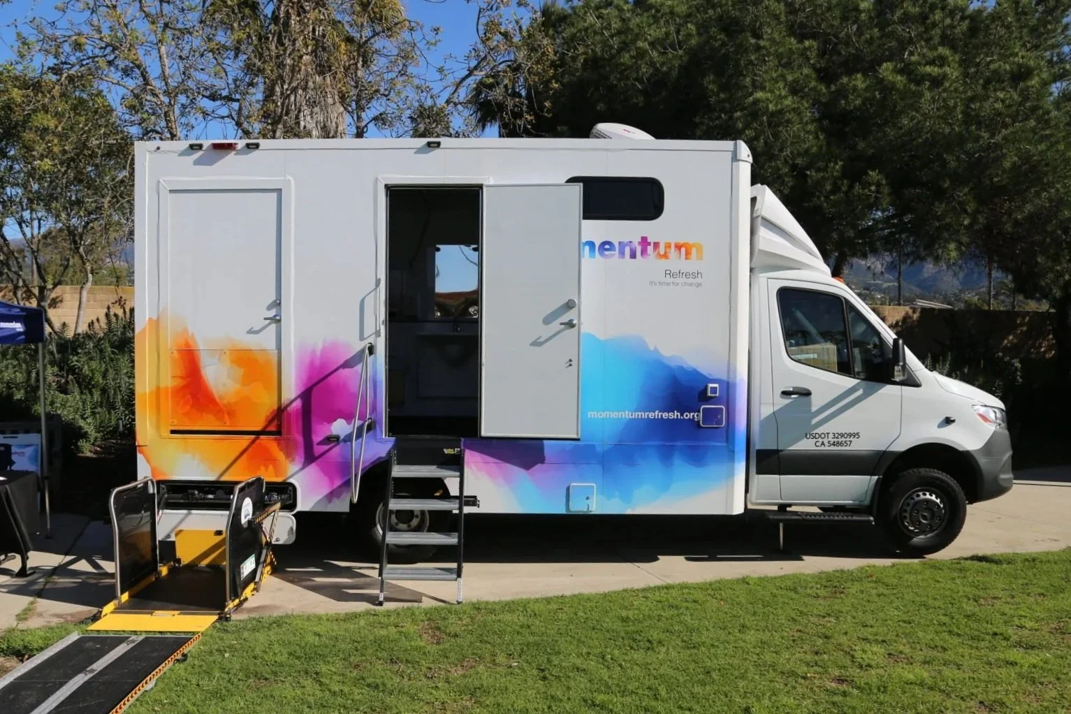 A mobile refresh unit with colorful branding parked on a driveway, accessible via a ramp and stairs.