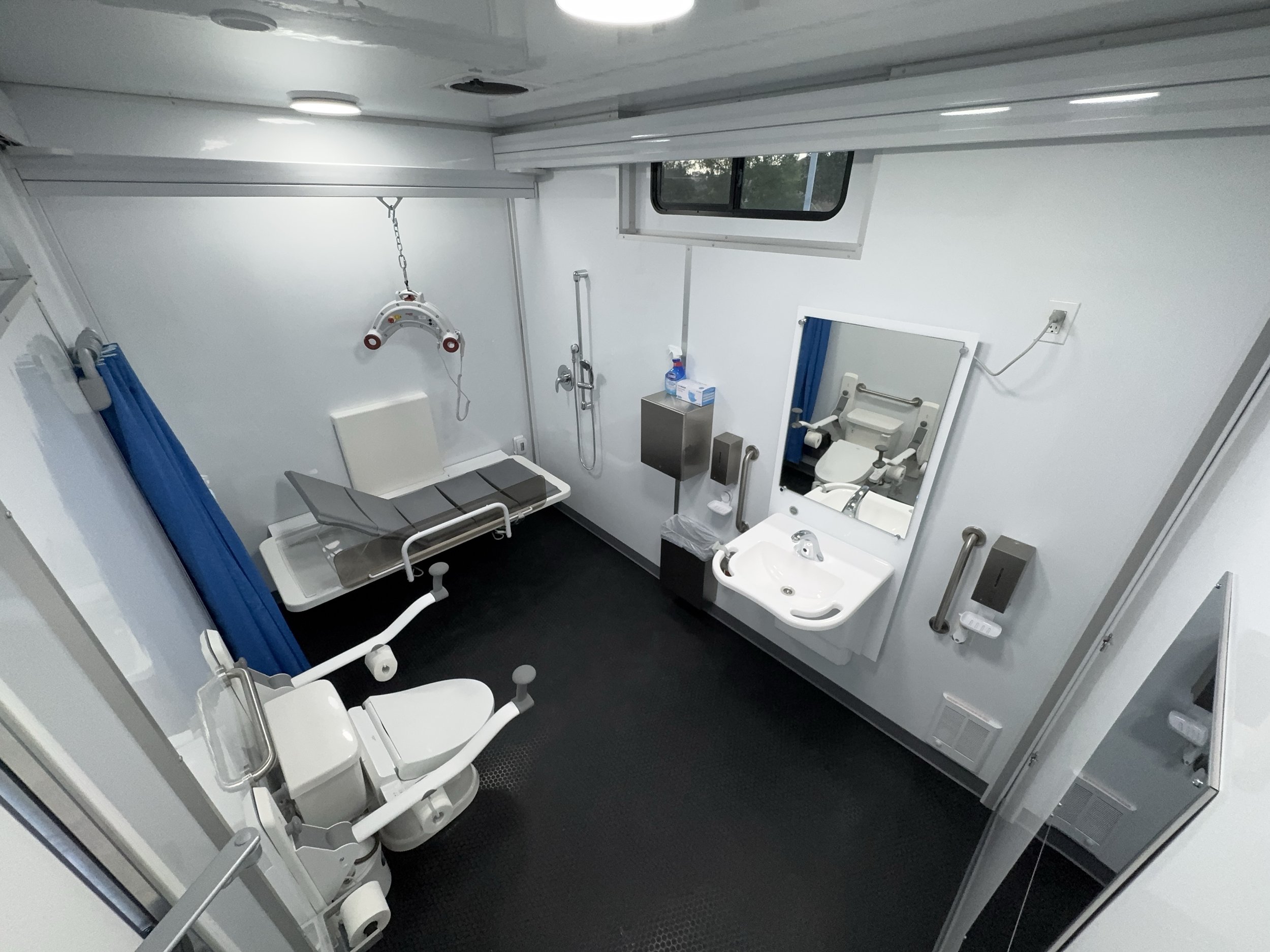 Hospital or medical examination room with a hospital bed, a wheelchair, a sink, a mirror, and medical equipment.