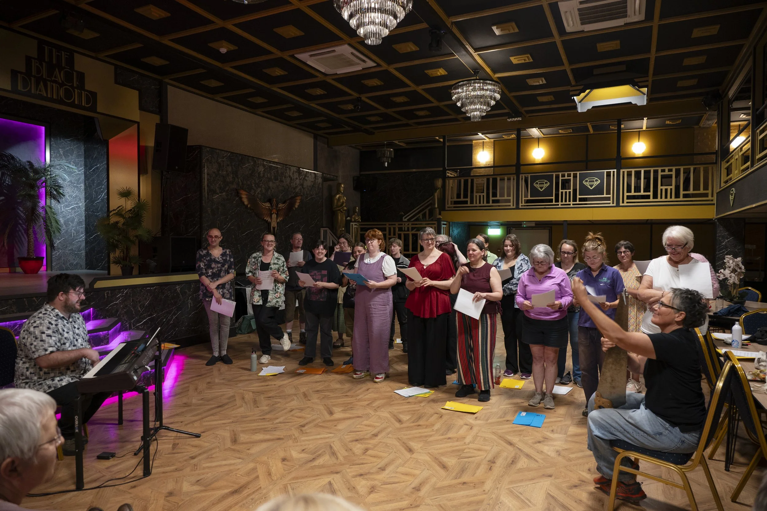 Wyrd Voices members performing with Matt at the piano and one member playing musical saw all in the art deco styled venue