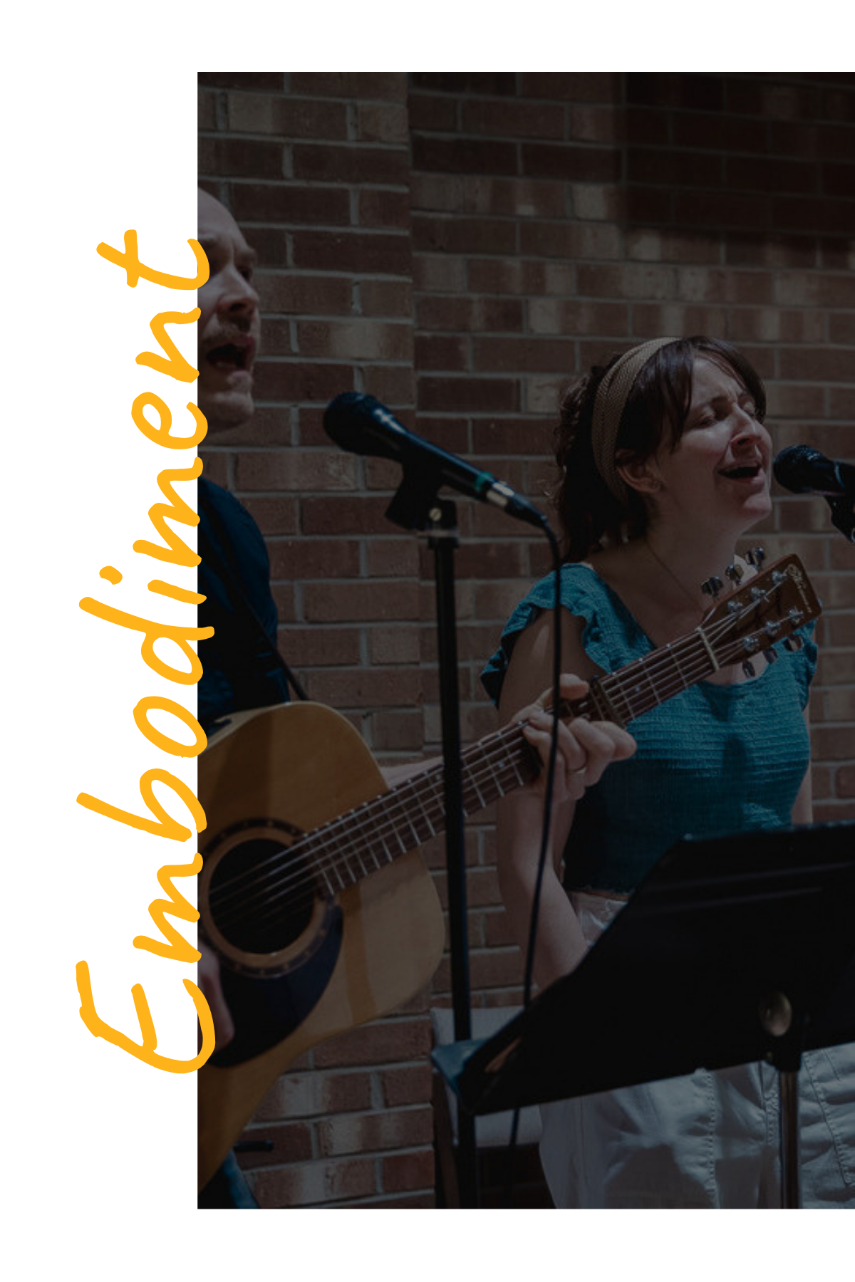 Two women singing and playing guitar, standing in front of a brick wall, with one woman playing guitar and the other singing into a microphone, possibly during a musical performance.