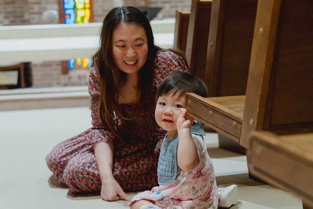 A woman and a young girl playing on the floor in a room with wooden furniture and a brick wall in the background.