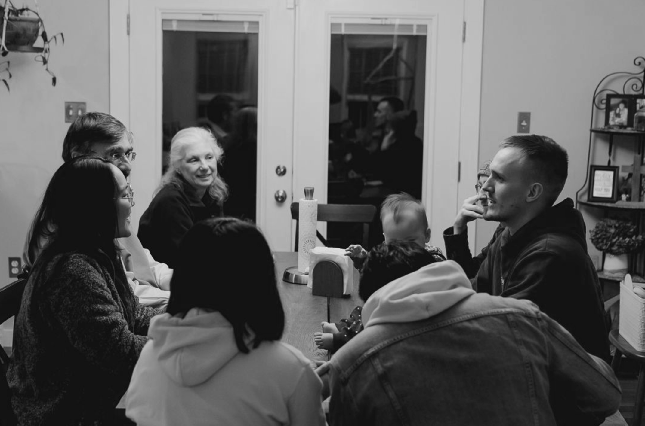 missio group meeting in durham. A group of people, including adults and children, sitting around a dining table in a cozy home kitchen, smiling and engaging in conversation.