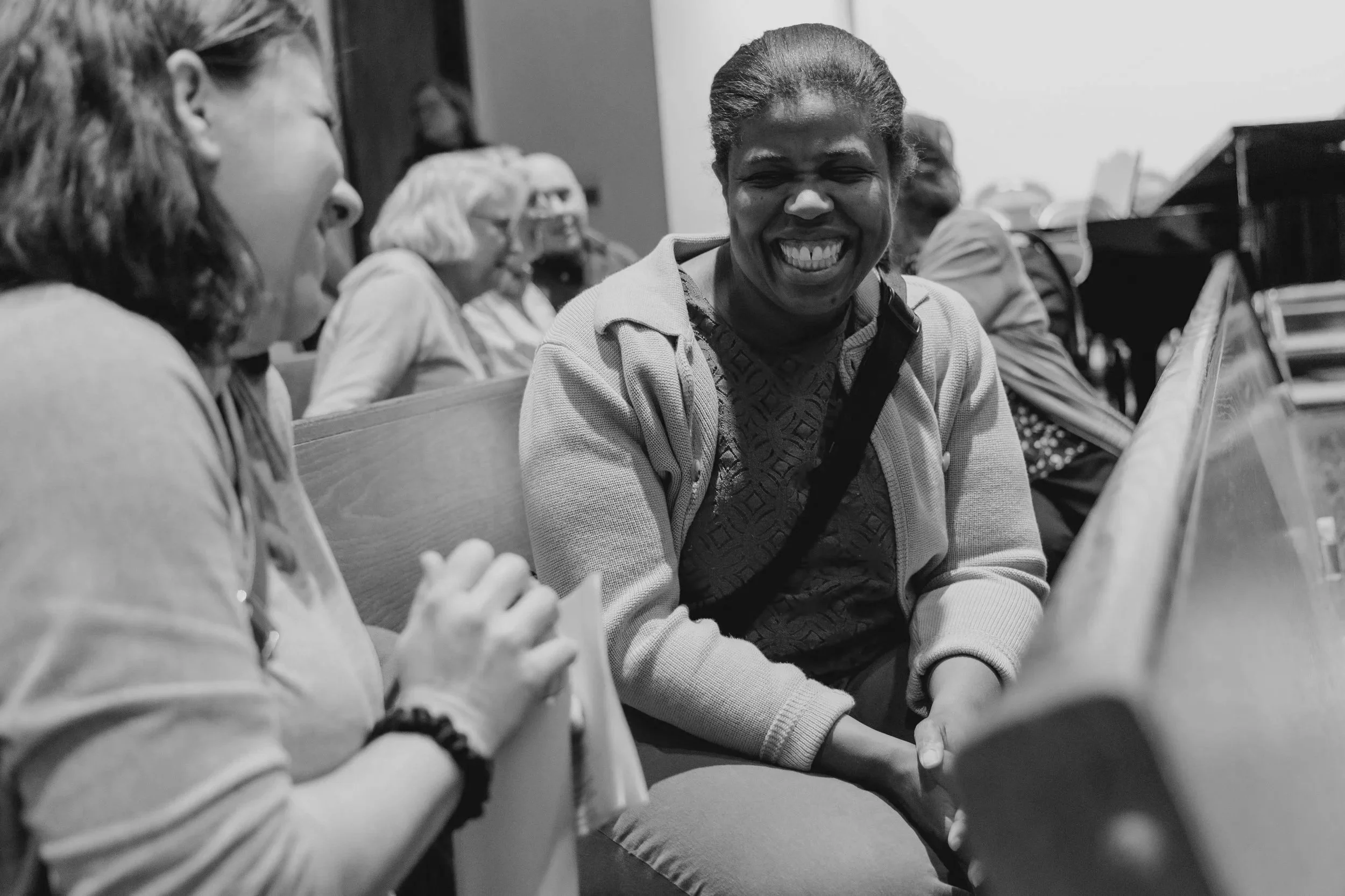 A group of women at missio durham's service, seated in a row, smiling and laughing together in an indoor setting.