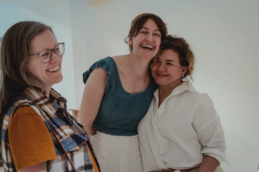 Three women sharing a joyful moment, smiling and laughing together indoors.