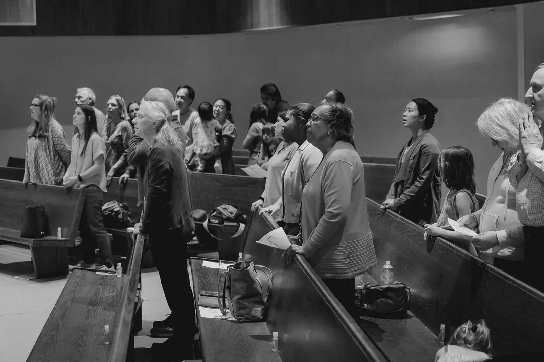 People standing in church pews, engaged in prayer or reflection during a service.