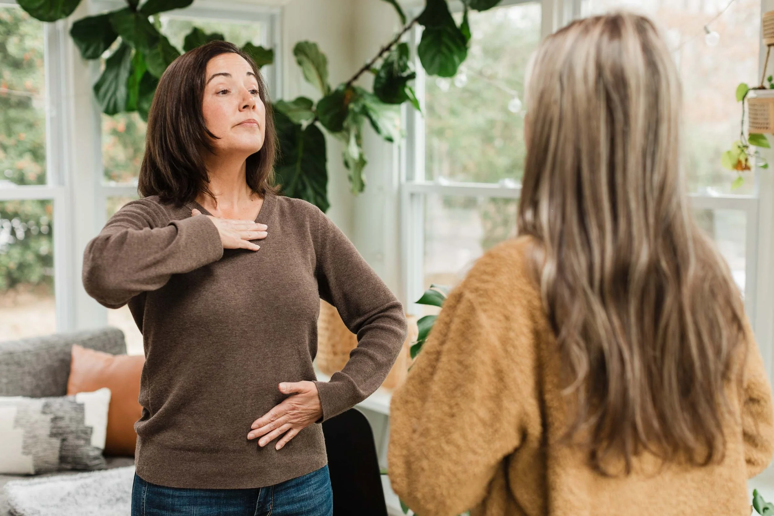 Vocal coach, Kristen Calhoun, in a brown sweater, demonstrates breathing technique to her student.