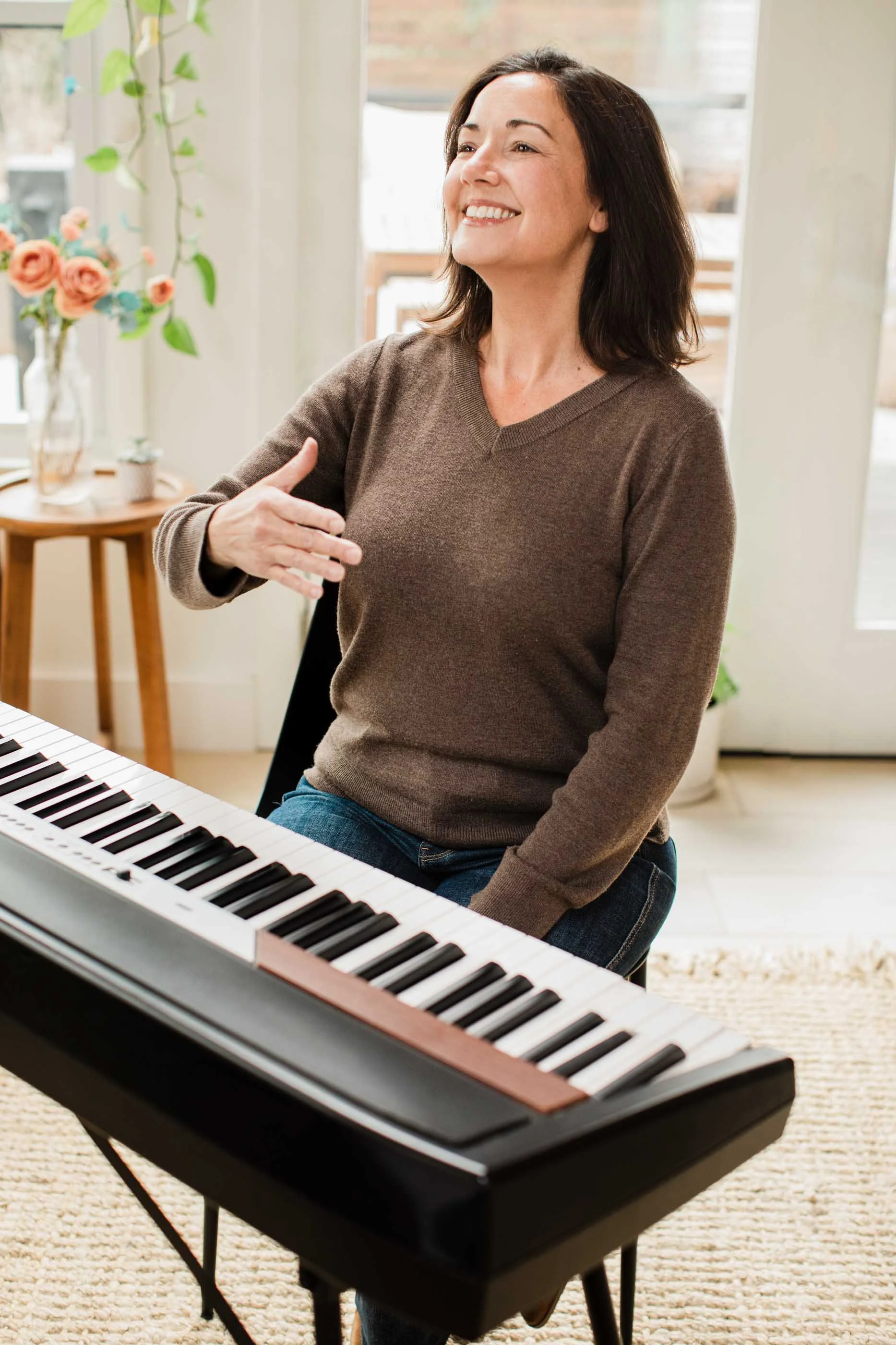 Vocal coach, Kristen Calhoun, sit behind her keyboard while conducting a vocal lesson in a bright, cozy room.