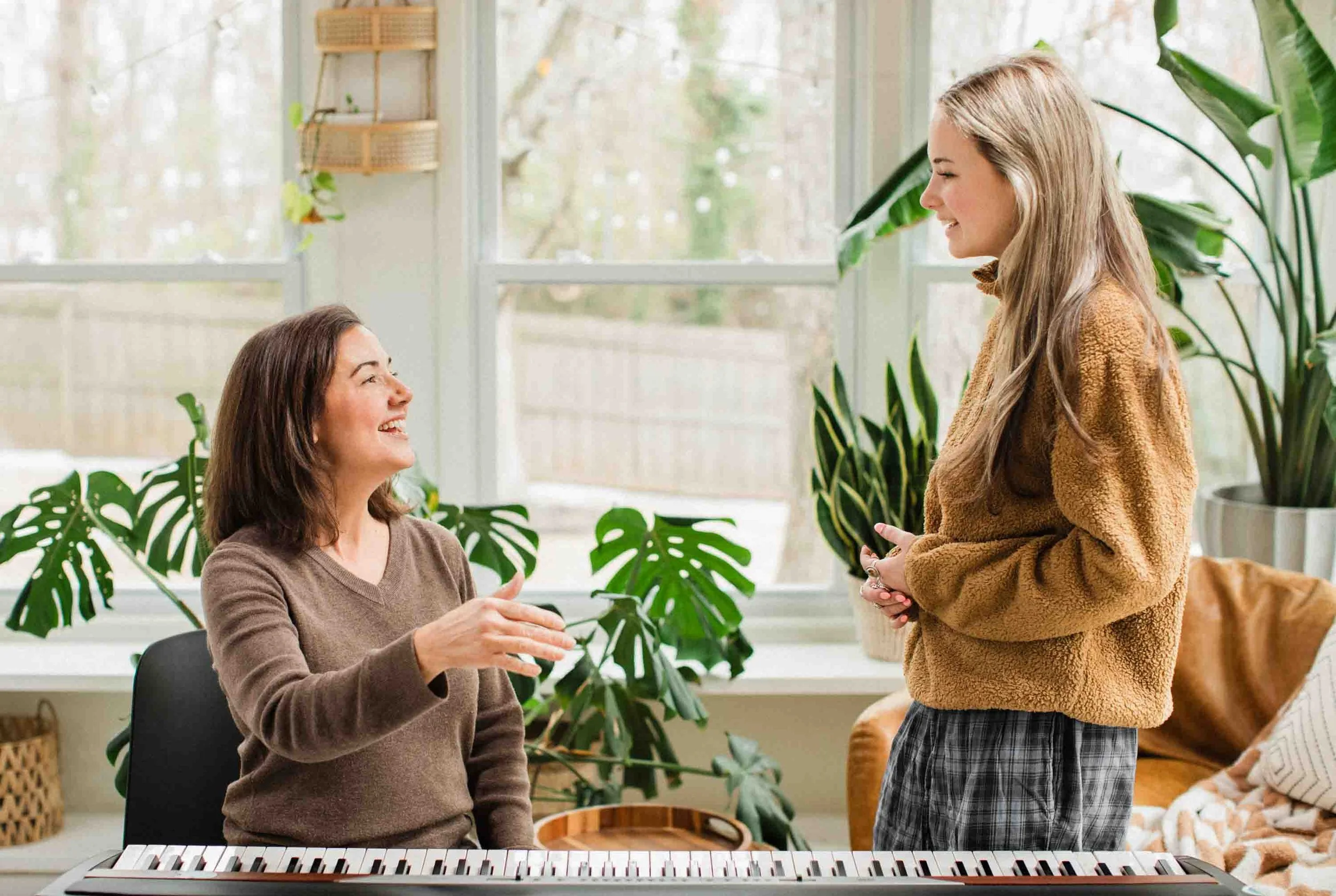 Greenville vocal coach sits behind keyboard while laughing with her student.