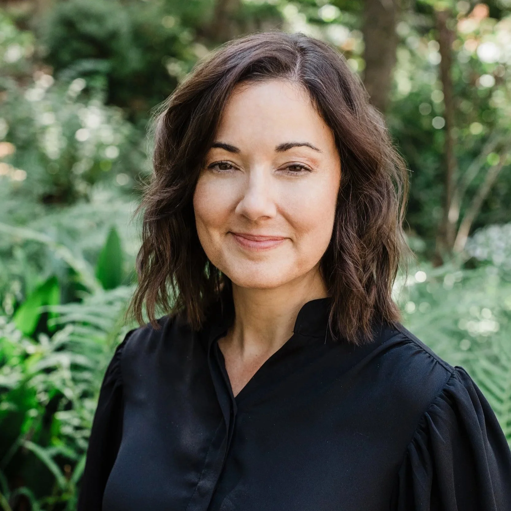 Portrait of Kristen Calhoun, speech therapist and vocal coach, smiling in a lush green garden.