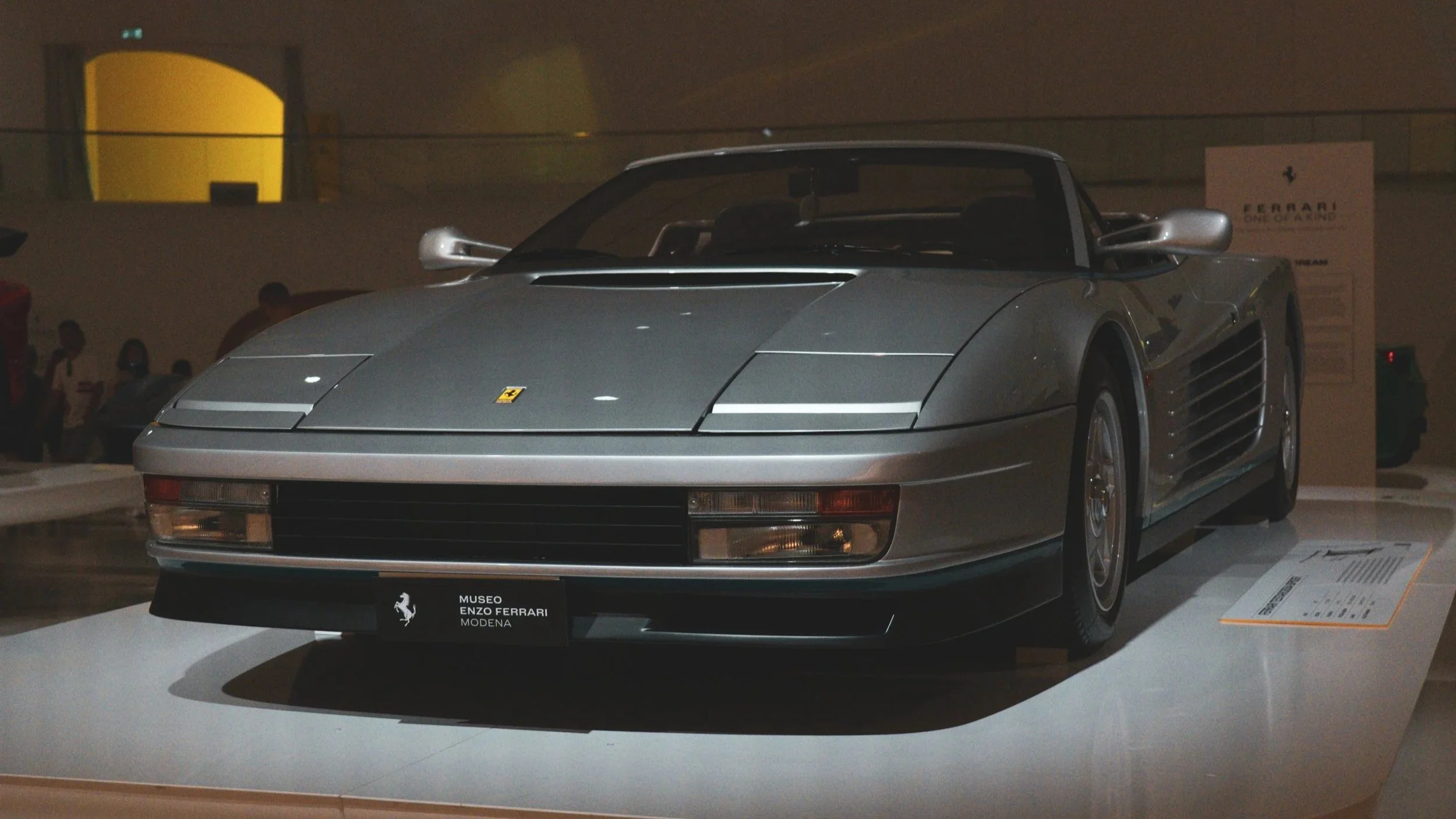A silver Ferrari sports car on display at a museum exhibit.
