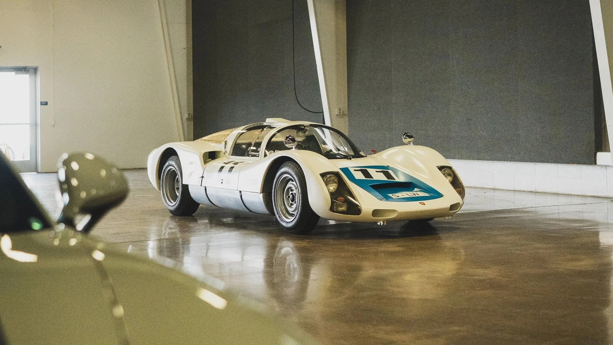 A vintage race car inside a modern exhibition space with black walls.