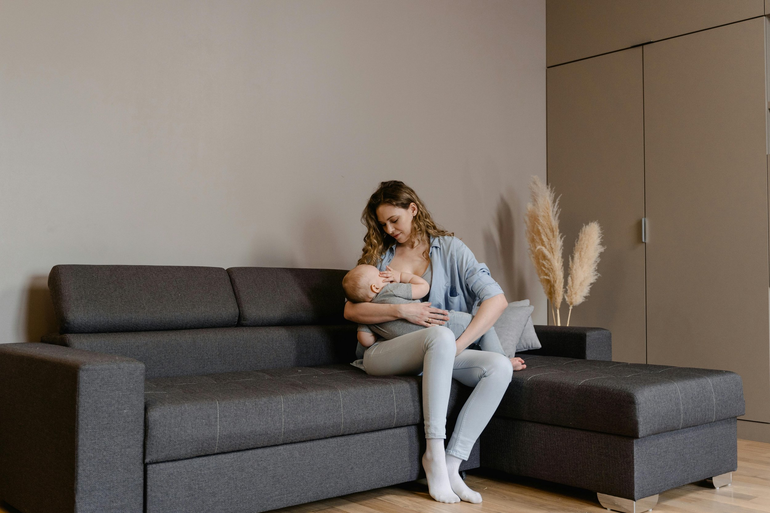 Mother breastfeeding baby on couch in calm home setting — postpartum bonding and adjustment period.