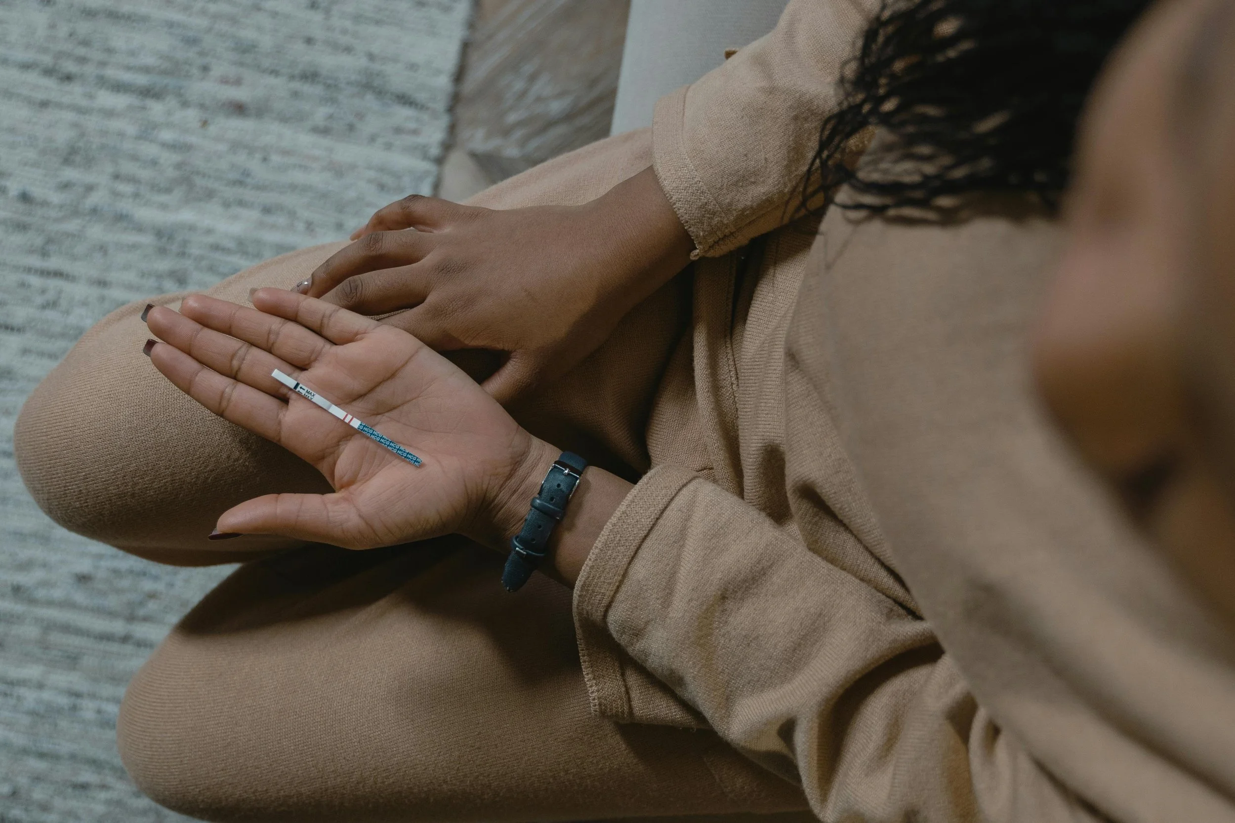 Person holding positive pregnancy test while sitting on floor — unexpected pregnancy feelings and anxiety.