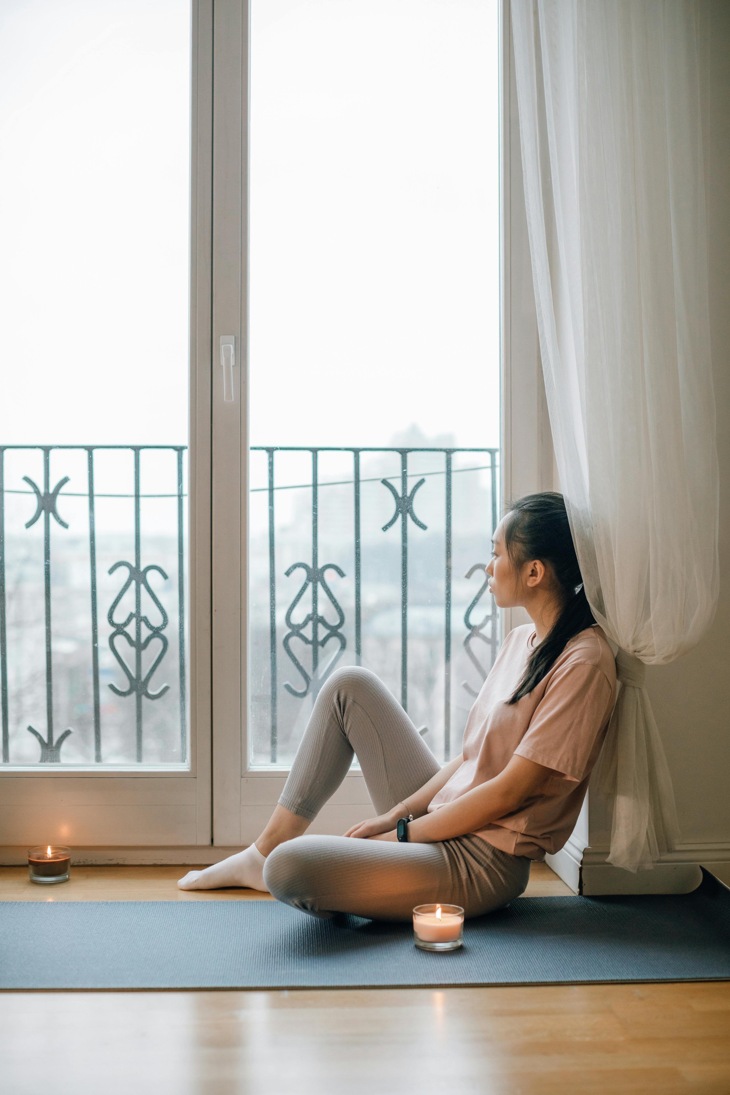 Woman sitting on yoga mat near window with candles — mindfulness and nervous system regulation.