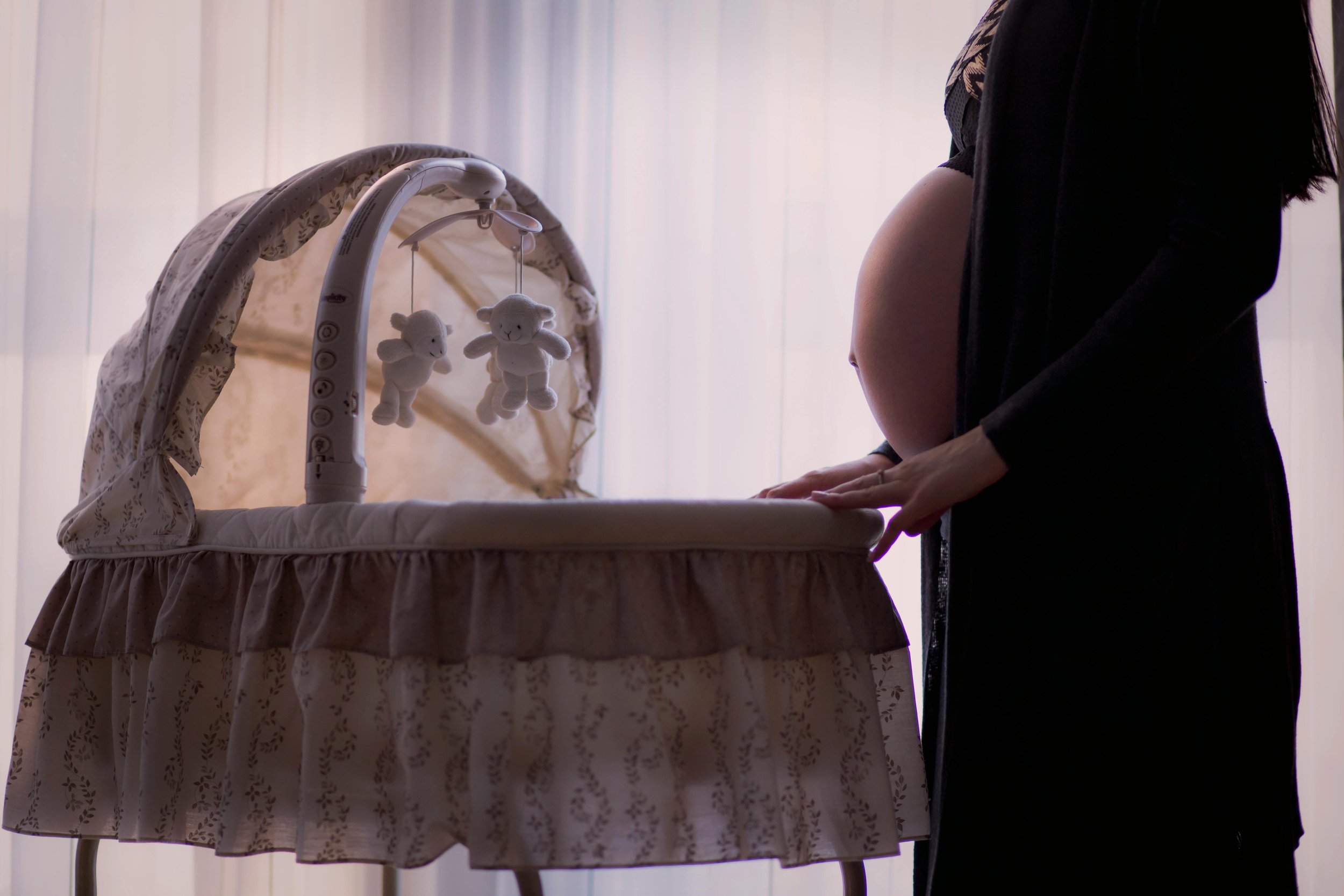 Pregnant woman preparing nursery beside bassinet — emotional transition into motherhood.