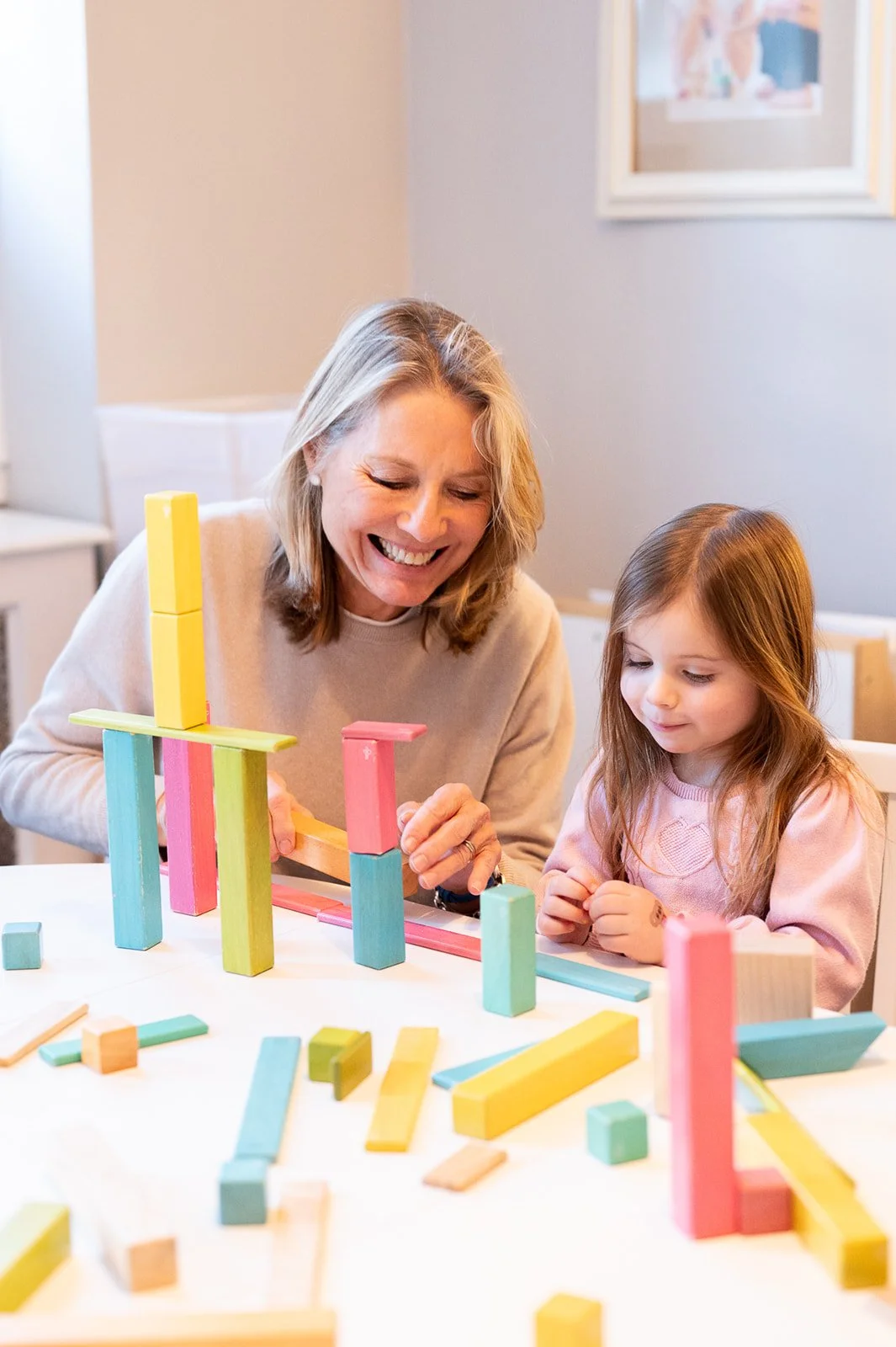 A woman and a young girl playing with colorful wooden building blocks on a table.