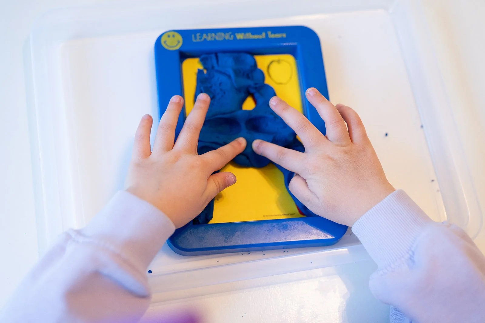 Child's hands pressing blue modeling clay on a yellow chalkboard labeled 'LEARNING Without Limits'.