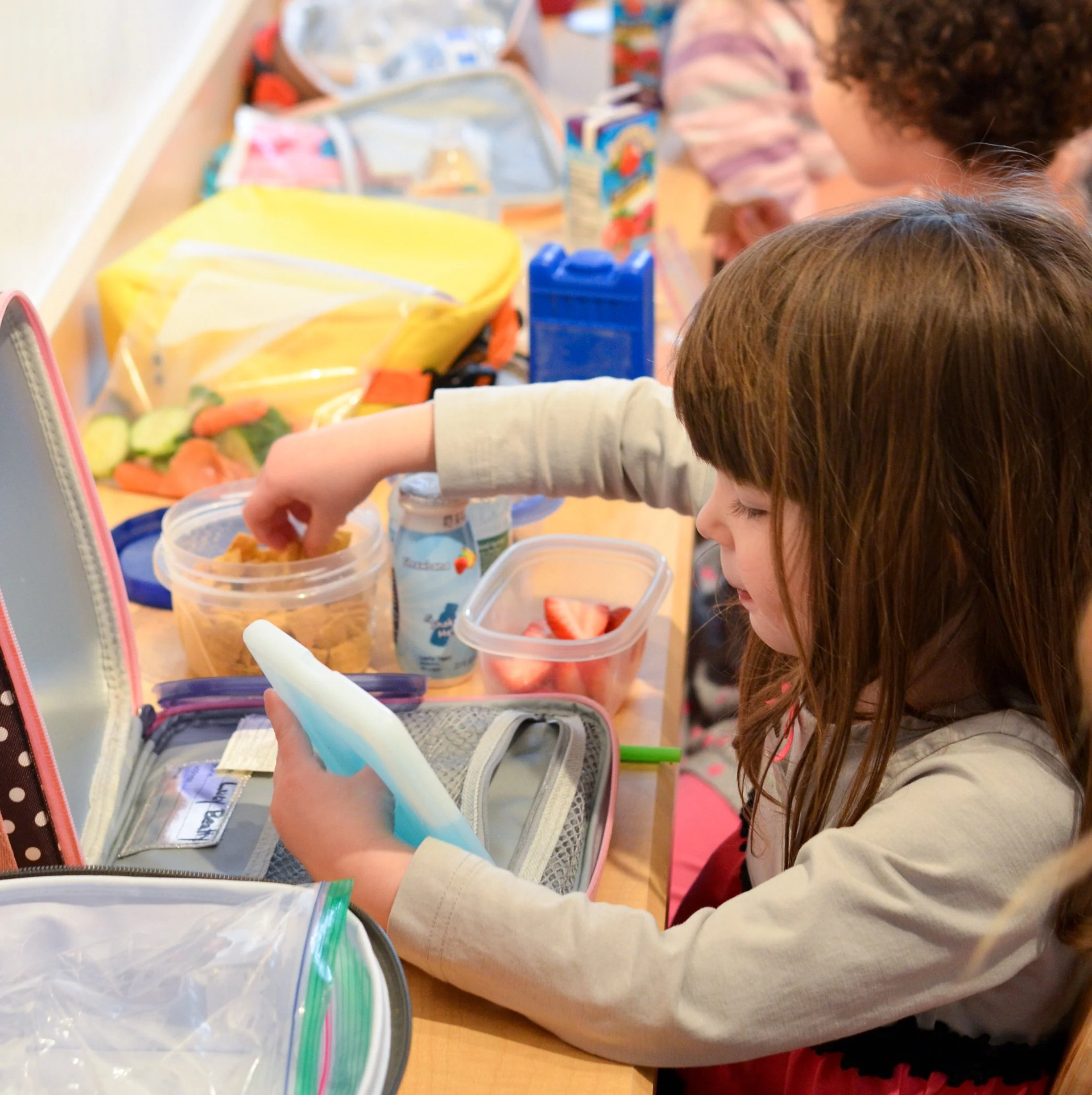 Children preparing snacks with various food containers and ingredients on a table.