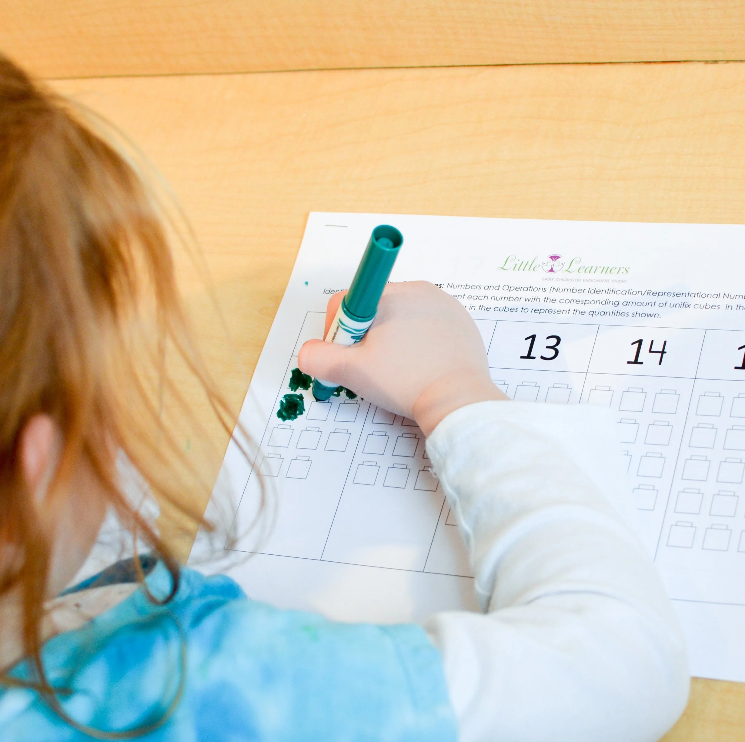 Child coloring on a worksheet with a green marker, learning numbers and quantities.