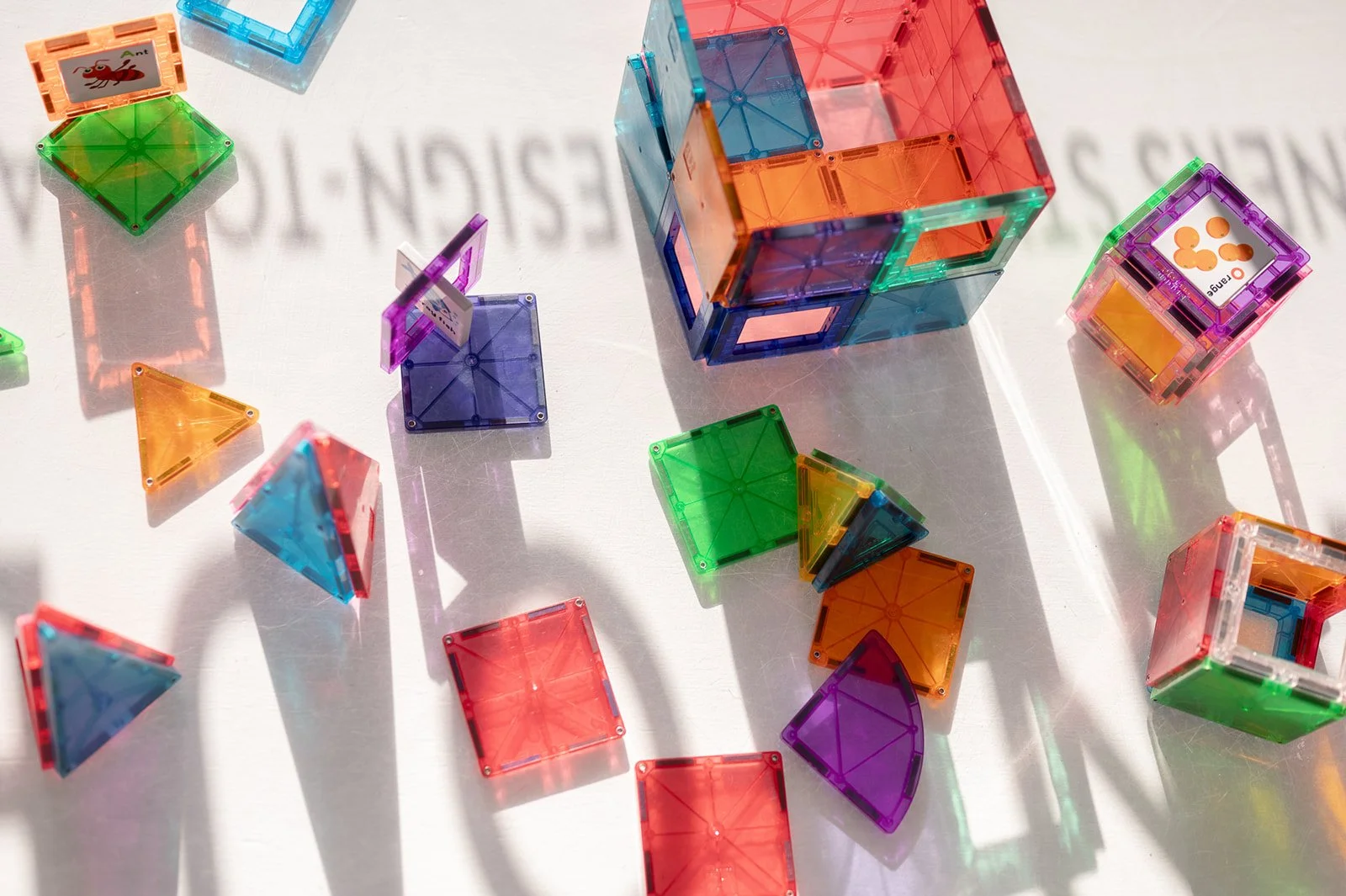 Colorful magnetic building blocks scattered on a white surface, with some assembled into cubes and other shapes, casting shadows.