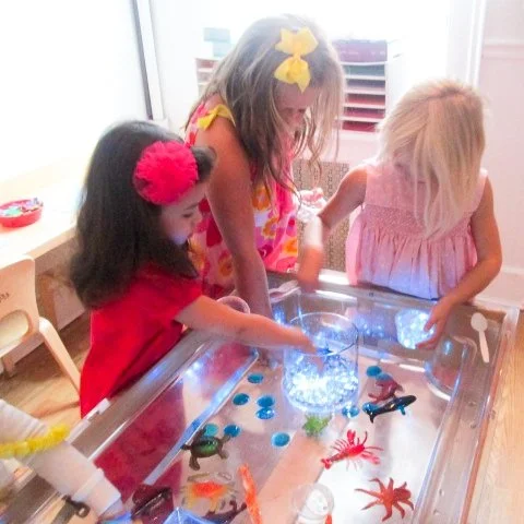 Three young girls playing an air hockey game with cartoon crab and lobster designs on the surface.