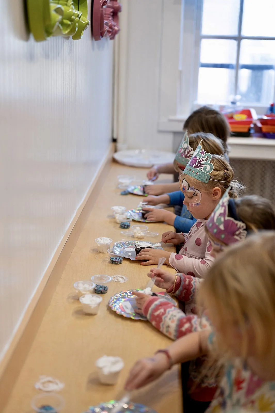 Children wearing unicorn headbands decorating cupcakes at a party table.