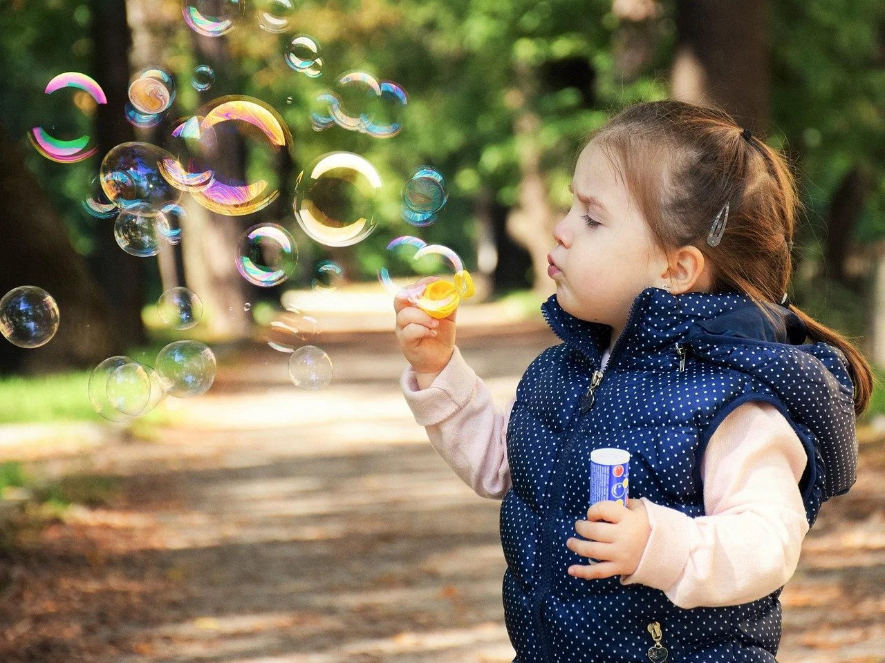 A young girl blowing bubbles in a forested park.