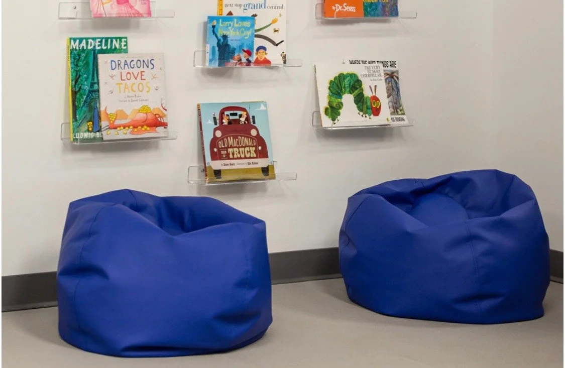Two blue bean bag chairs in front of a white wall with bookshelves holding children's books.