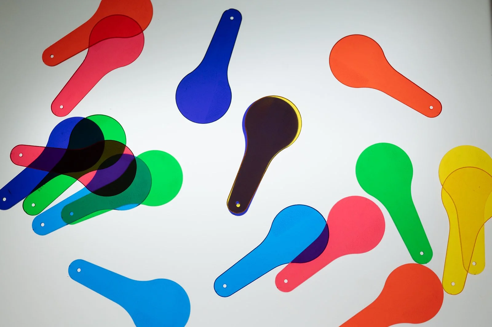 Several colorful plastic paddles in red, blue, green, yellow, black, and orange scattered on a white background.