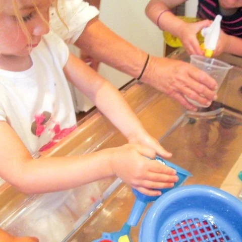 Children and an adult washing dishes together at a kitchen sink.