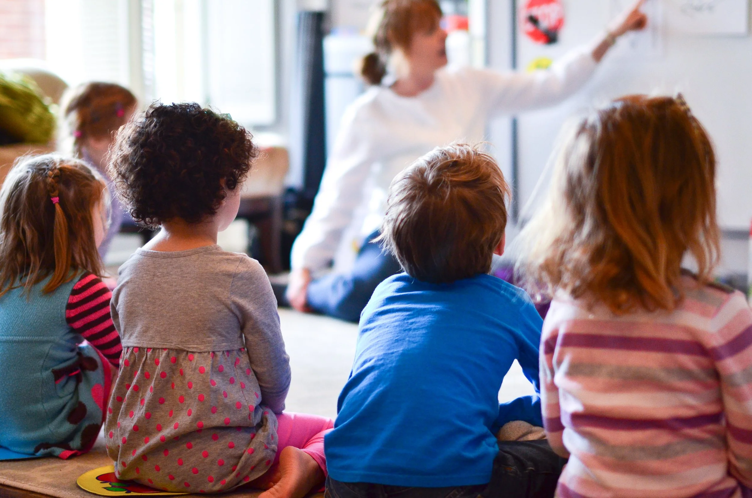 A teacher reading to a group of young children seated on the floor during a classroom activity.