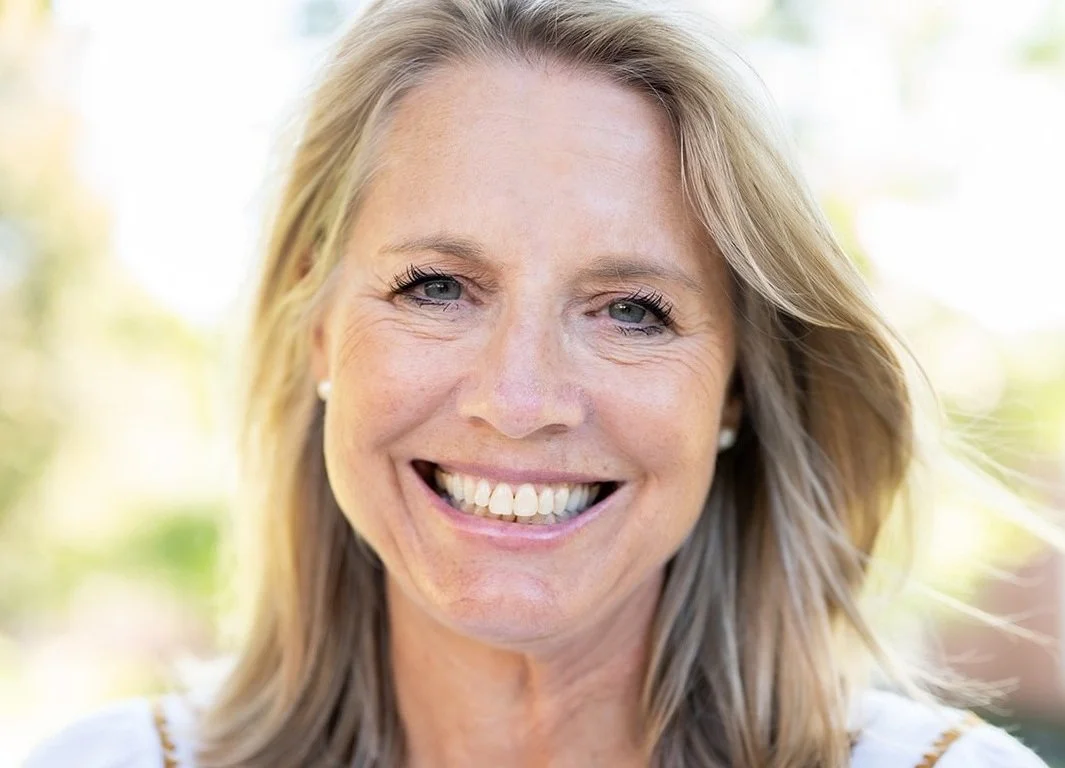 A woman with blonde hair smiling outdoors on a sunny day