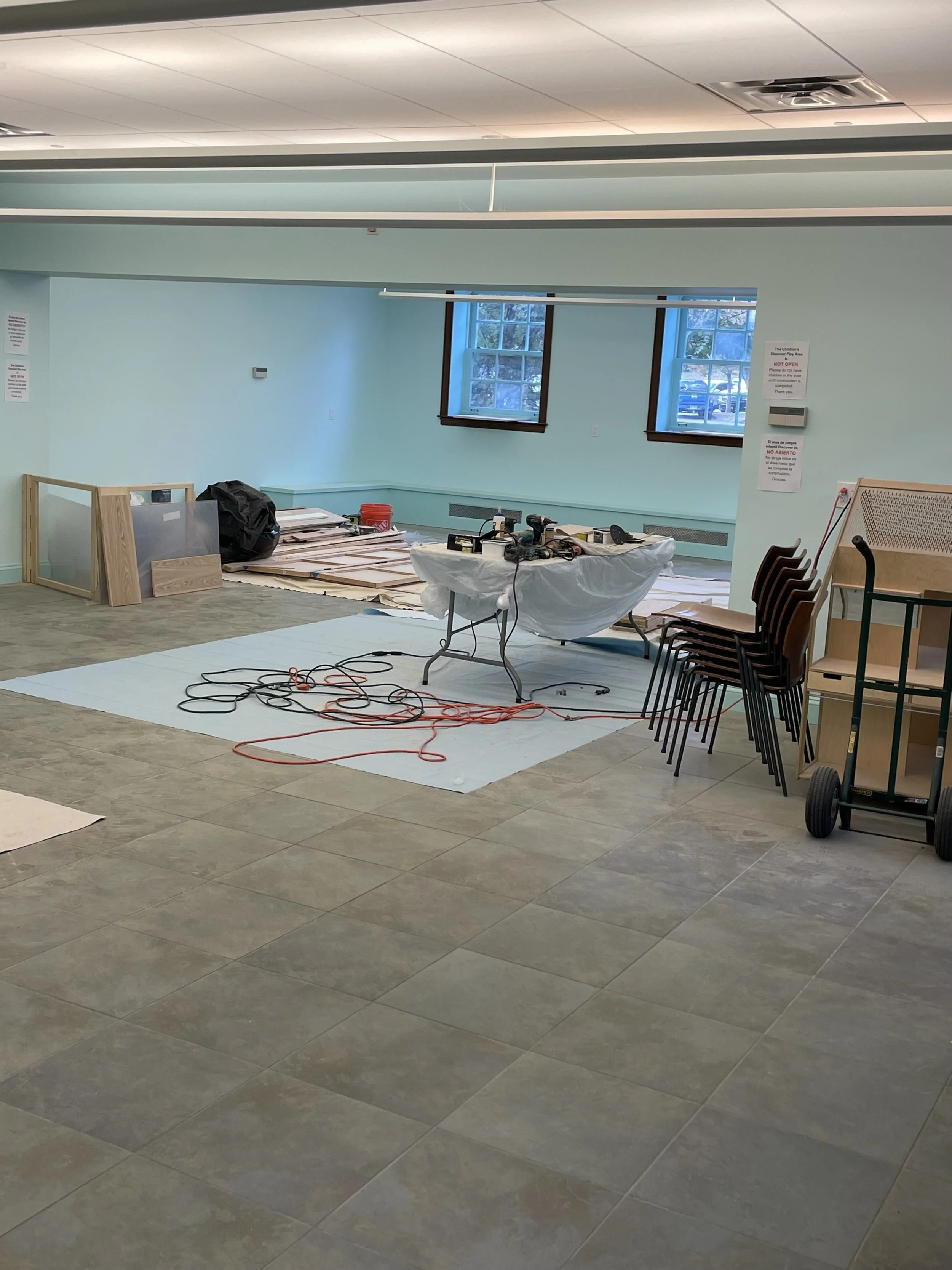 Room with construction tools, chairs stacked on top of each other, and construction materials on the floor and table.