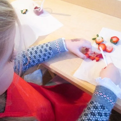 Child slicing strawberries at a table with strawberries and a knife.