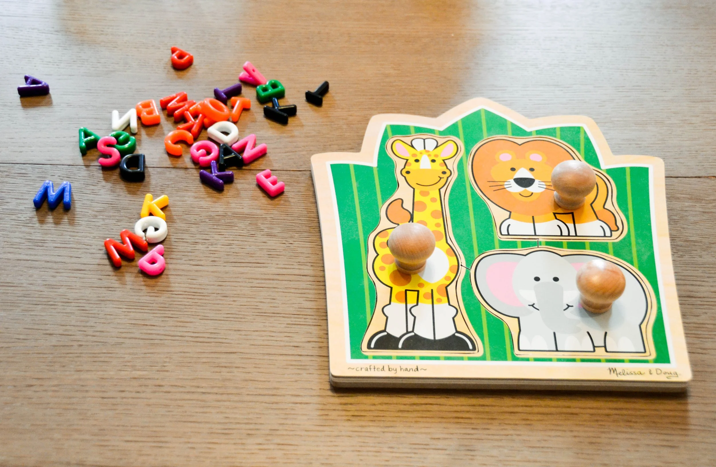 Colorful alphabet letter tiles and a wooden puzzle with a giraffe, lion, and elephant on a wooden table.