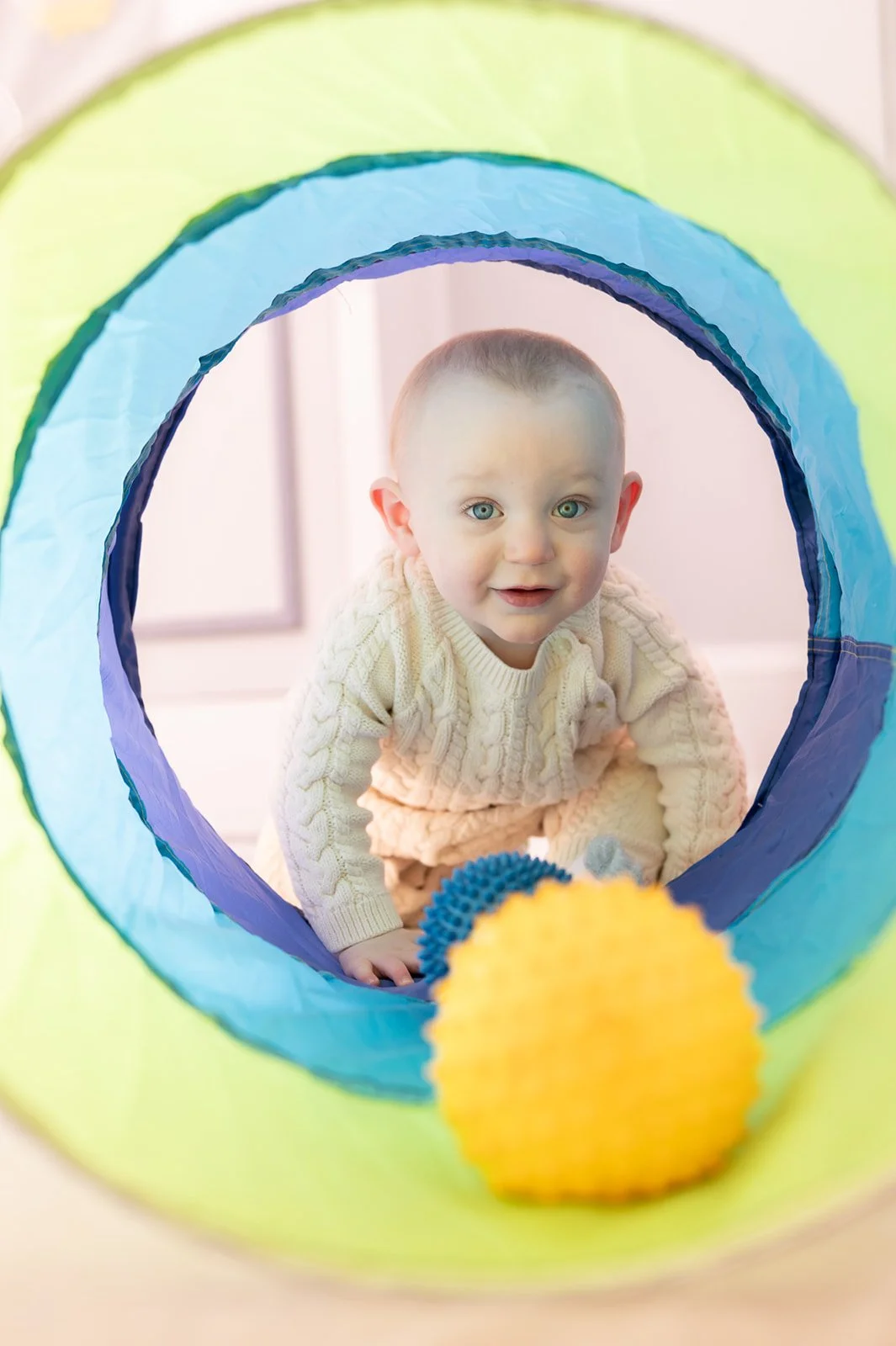 A young child crawling through a colorful play tunnel with soft textured balls nearby.