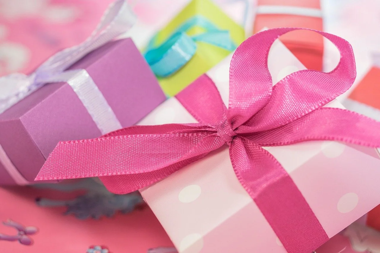 Close-up of colorful wrapped gifts with pink ribbons, featuring pink, purple, green, and white wrapping papers with various patterns.