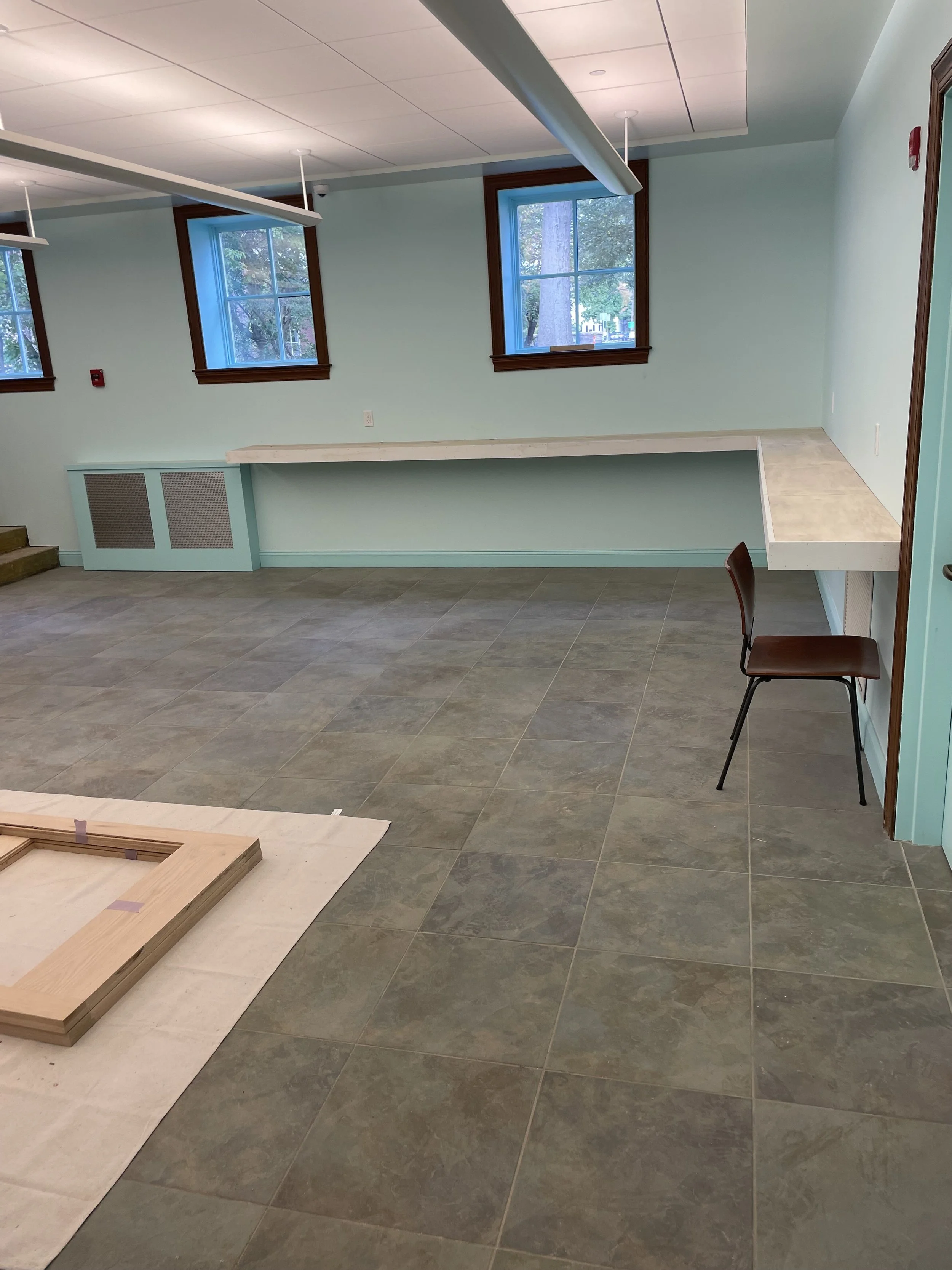 Empty room with mint green walls, three windows, a long white counter, and a single brown chair.